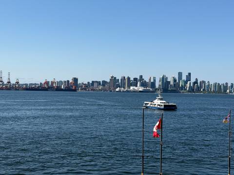 Vancouver skyline rises behind blue harbour waters with a ferry and Canadian flag in the foreground.