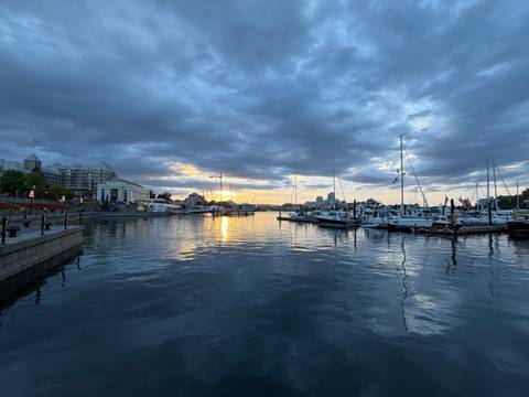 Boats moored in a calm harbour at sunset beneath dramatic clouds.