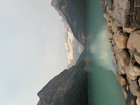 Turquoise glacial lake surrounded by rocky peaks and distant snowy mountains.