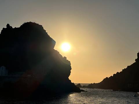 Sun setting behind jagged rock formations creating dramatic silhouettes over the sea.