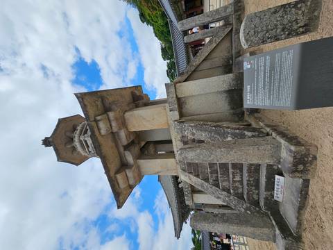 Stone pagoda monument within a temple complex with informational plaque under partly cloudy sky.