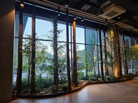 Modern hotel or building lobby with tall indoor trees and large floor-to-ceiling windows.