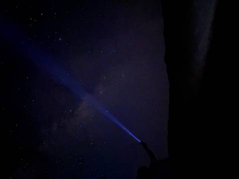Night desert scene with a person shining a blue flashlight beam toward a star-filled sky