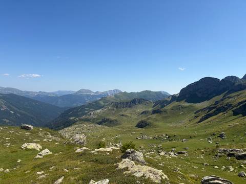Expansive panorama of rolling green valleys and distant peaks beneath a clear alpine sky.