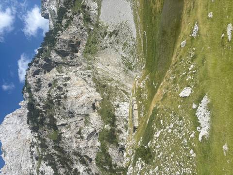 Sheer limestone cliffs tower above a narrow alpine valley with traces of old stone structures.
