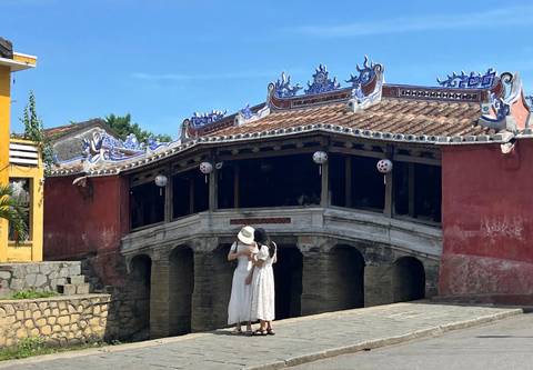 Two women in white dresses stand beside the Japanese Covered Bridge decorated with lanterns in Hoi An’s old quarter.