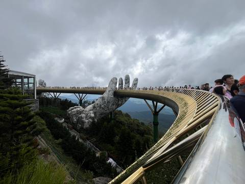 The curving Golden Bridge supported by giant stone hands stretches across misty mountains filled with tourists.