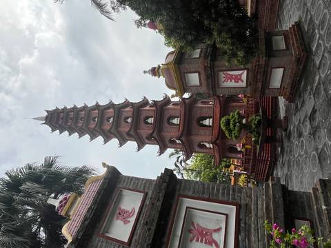 The slender brick Tran Quoc Pagoda rises between ornamental gateways against a lightly clouded sky in Hanoi.
