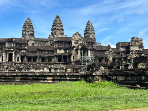 The iconic towers and galleries of Angkor Wat stand majestically with restoration scaffolding against a blue sky.