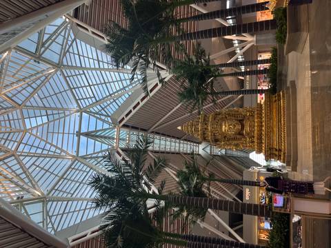 Interior of a modern airport terminal with a large golden statue beneath soaring glass and steel architecture.