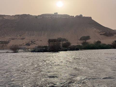 View across the Nile River toward a sandy hill crowned by a mausoleum under hazy afternoon light.