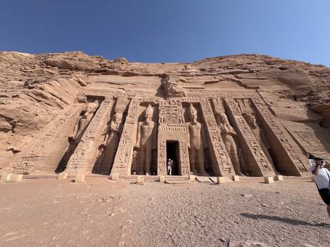 The rock-cut façade of Abu Simbel's Temple of Nefertari towers above two small visitors at the entrance.
