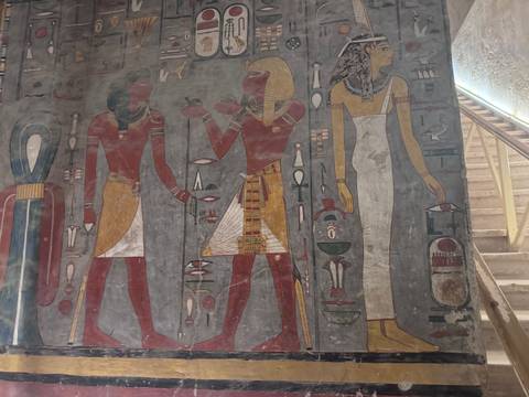Colorful wall paintings of Egyptian deities and symbols inside an ancient tomb corridor.