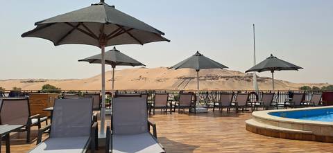 Sun deck with loungers and umbrellas overlooking golden desert hills.