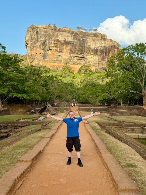 Traveler standing with arms outstretched on approach path to Sigiriya rock fortress ruins