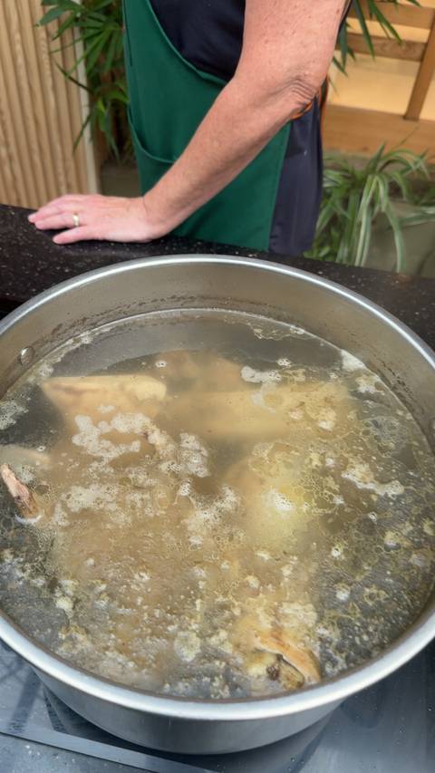 Large pot of cloudy simmering broth with bones and fat floating on top.