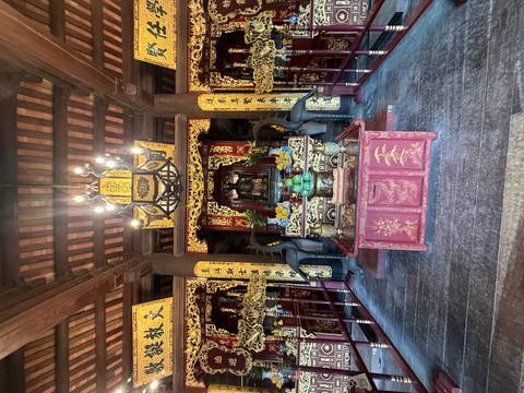 Interior of ornate Vietnamese temple with red lacquered altar and golden decorations.