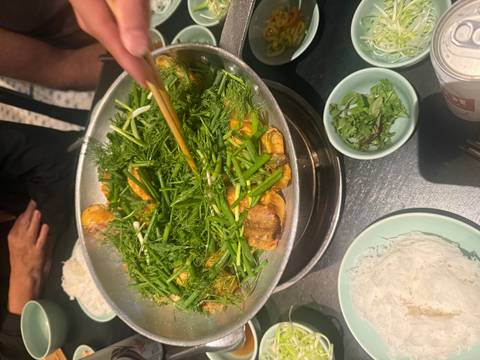 Vietnamese fish dish sizzling in a pan filled with fresh dill and herbs being stirred with chopsticks.