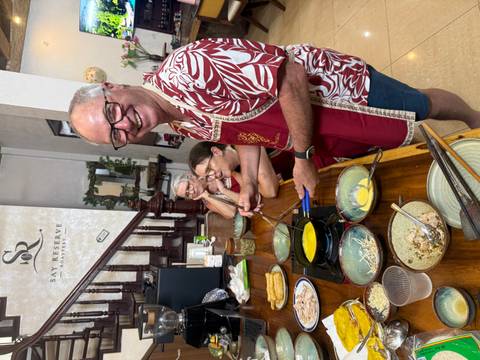 Smiling participant in cooking class wearing apron, surrounded by ingredients on a wooden table.