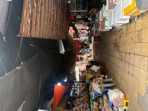 Covered wet market aisle with stalls, tarps overhead and locals sitting on plastic chairs.
