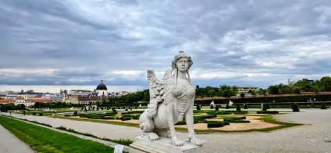 Stone sphinx statue overlooks the manicured lawns of Belvedere Gardens under a brooding sky.