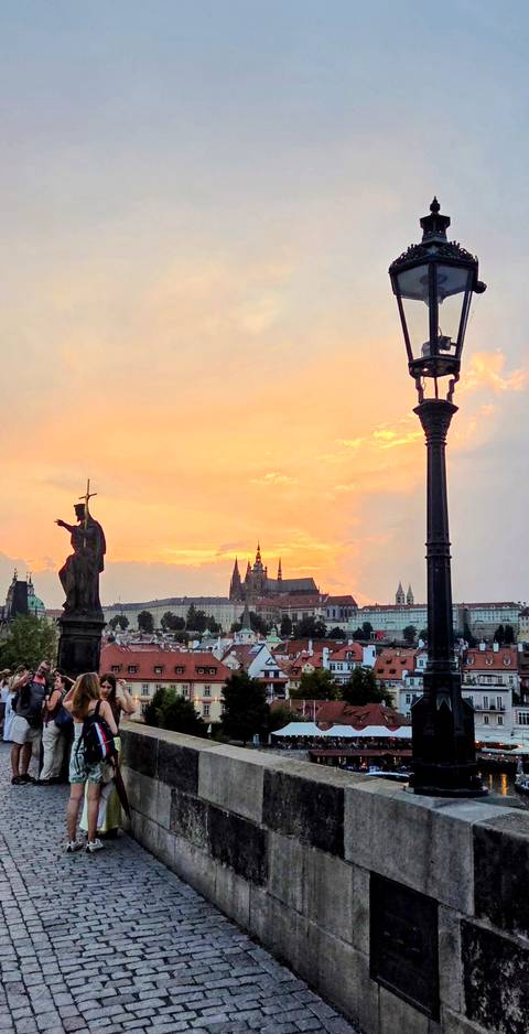 Silhouetted statues on Charles Bridge frame Prague Castle beneath a fiery sunset sky.