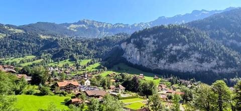 Sunlit Swiss village nestles in a green valley beneath towering cliffs and alpine peaks near Lauterbrunnen.