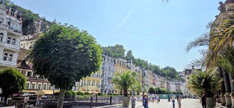 Colorful riverside façades and a leafy promenade bustle with tourists in Karlovy Vary.