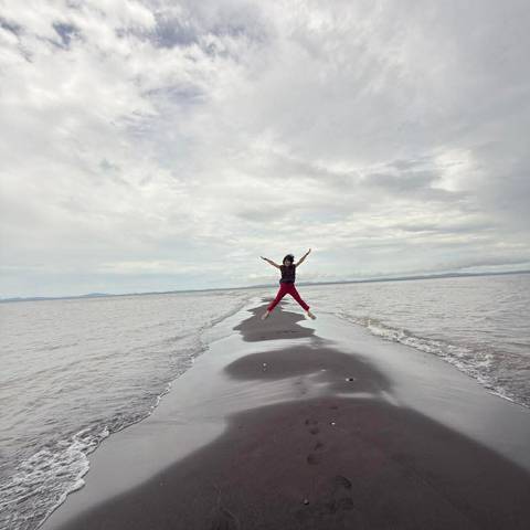 Traveler jumps joyfully on a narrow sandbar stretching into a vast lake or sea.