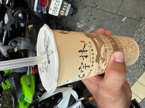 Hand holding a cup of Taiwanese bubble tea on a scooter-lined city street.