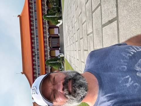 Man takes selfie in front of ornate Buddhist temple with orange tiled roof.