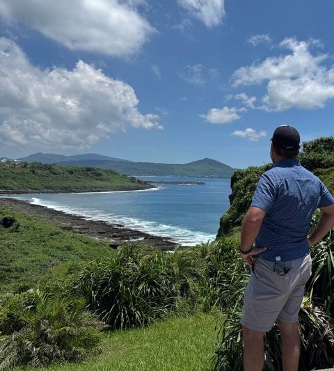 Traveler stands on cliffside overlooking blue sea and green hills of Kenting coast.