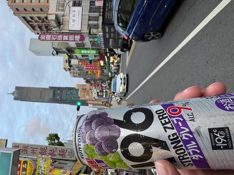 Hand holding grape chu-hi can with busy Kaohsiung street and 85 Sky Tower in background.