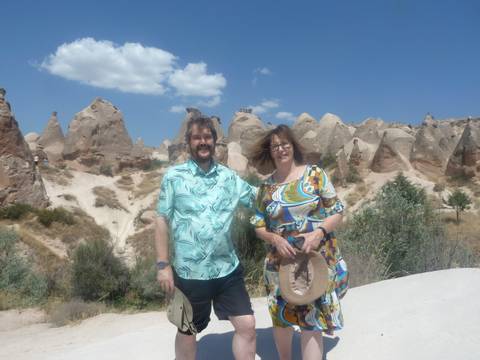 Couple stands in front of whimsical rock formations and fairy chimneys under a bright Cappadocia sky.