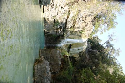 Serene waterfall cascades over rock ledges into a turquoise pool surrounded by green trees.