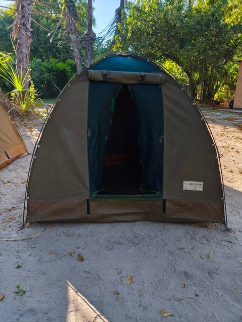 Close view of the open doorway of a small canvas safari tent on sandy ground.