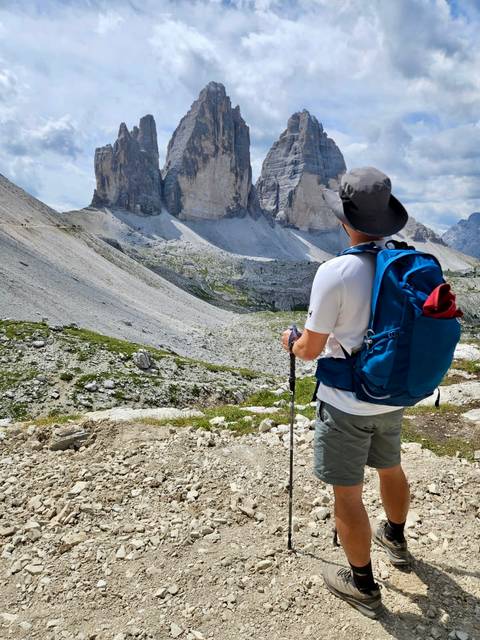 Back-view of hiker with trekking poles gazing up at the stark limestone walls of Tre Cime di Lavaredo.