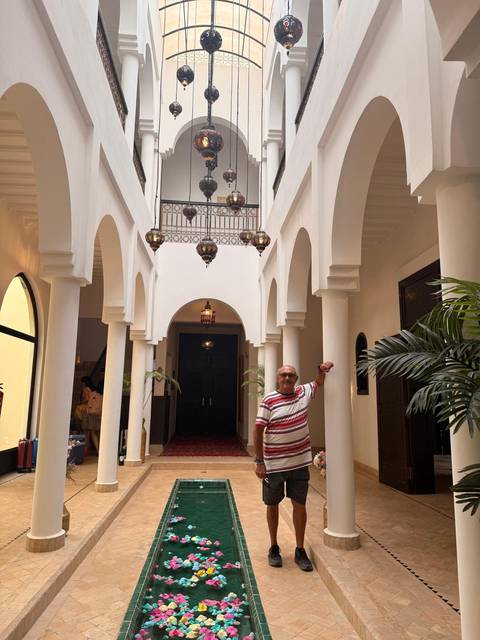 A man poses in the arched hallway of a traditional Moroccan riad with hanging lanterns.