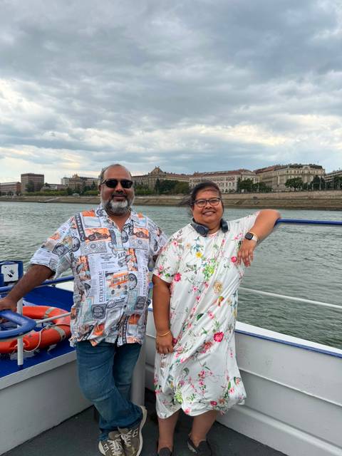 A couple on a boat deck with Budapest’s riverside architecture visible across the Danube.