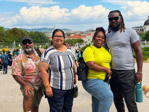 Four travellers pose in a formal garden with Vienna’s skyline and palace spires in the background.