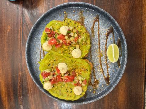 Colourful plate of avocado toast topped with diced tomato, sesame and lime wedge.