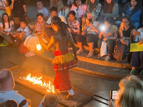 Bare-chested performer walking over flames during a traditional Sri Lankan fire dance while audience looks on