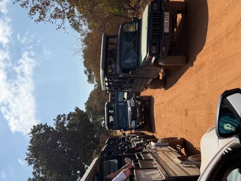 Line of open-air safari jeeps driving on a dusty track under a bright sky