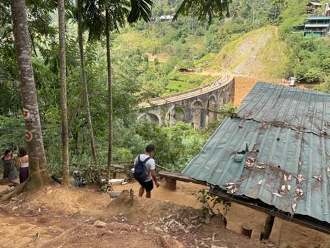 View down jungle slope toward the iconic Nine Arches Bridge with a hiker descending a dirt path