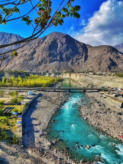 Turquoise river flows beneath a bridge through a steep rocky valley with fresh spring foliage.