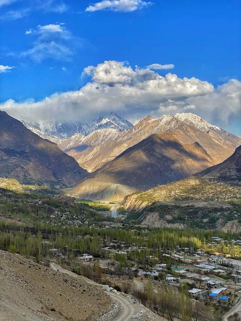 Expansive mountain panorama with rugged peaks dusted in snow and a broad valley below under dramatic clouds.