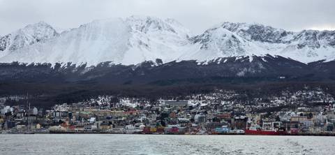 Panoramic view of Ushuaia town backed by dramatic snowy mountains, seen from the water.