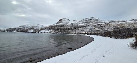 Quiet snowy shoreline curving around a still lake beneath overcast winter skies.