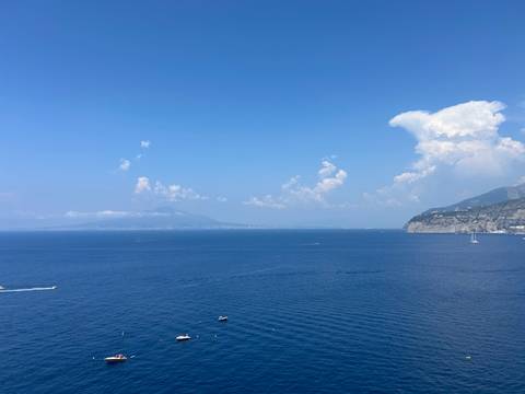 Expansive view over the Bay of Naples with Mount Vesuvius faintly visible on a hazy summer day.