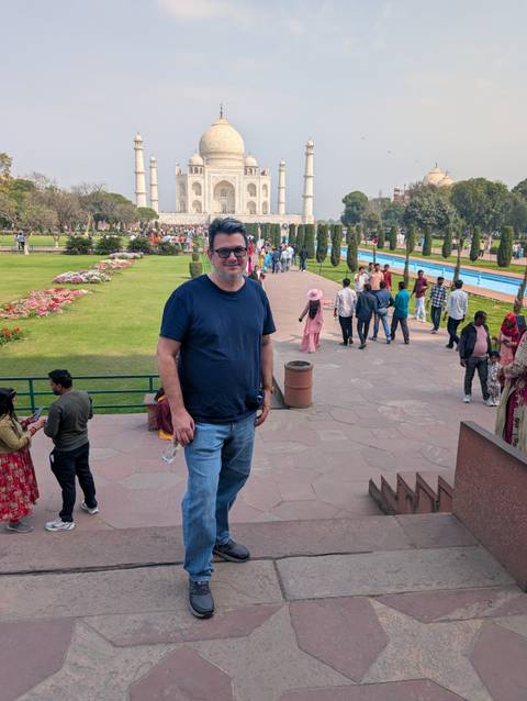 Visitor poses on steps overlooking manicured gardens leading toward the Taj Mahal’s white marble dome.